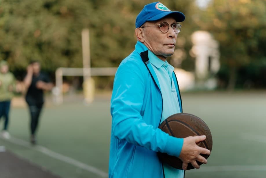 藍色帽子、藍色衣服、藍色外套的老先生在籃球場抱著籃球