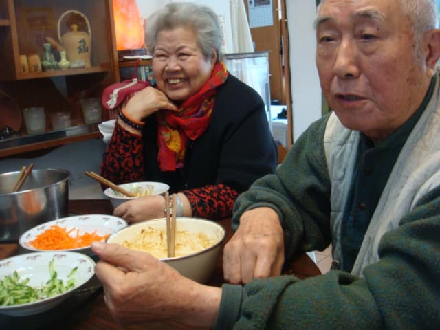老爺爺老奶奶坐在桌邊一起吃桌上的菜餚