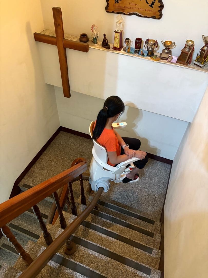 牆上有十字架裝飾且有身著橘色衣服的女子乘坐樓梯升降椅.jpg